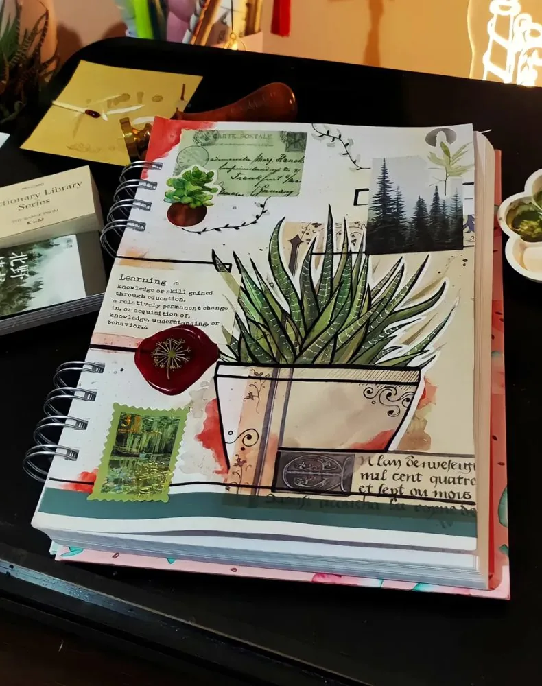 Caderno de artes aberto com colagens e o desenho de um vaso de planta