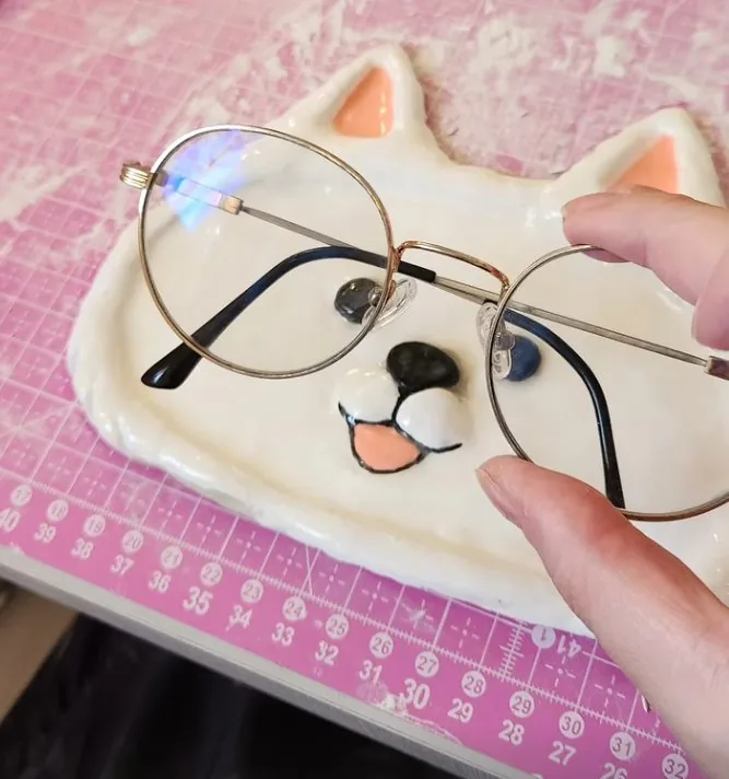 Porta-óculos de cerâmica branca em forma de cachorrinho, com um par de óculos apoiado