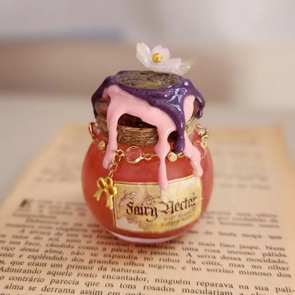 Pote de vidro com rótulo Fairy Nectar e tampa coberta de cera rosa e roxa escorrendo, sobre um livro aberto