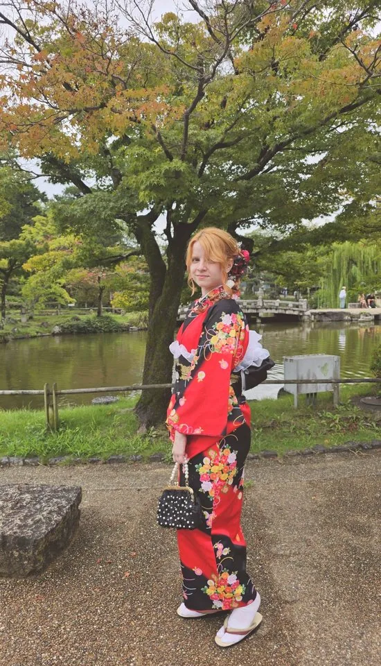 Bruna de quimono vermelho num jardim japonês em Quioto, ao lado de um lago