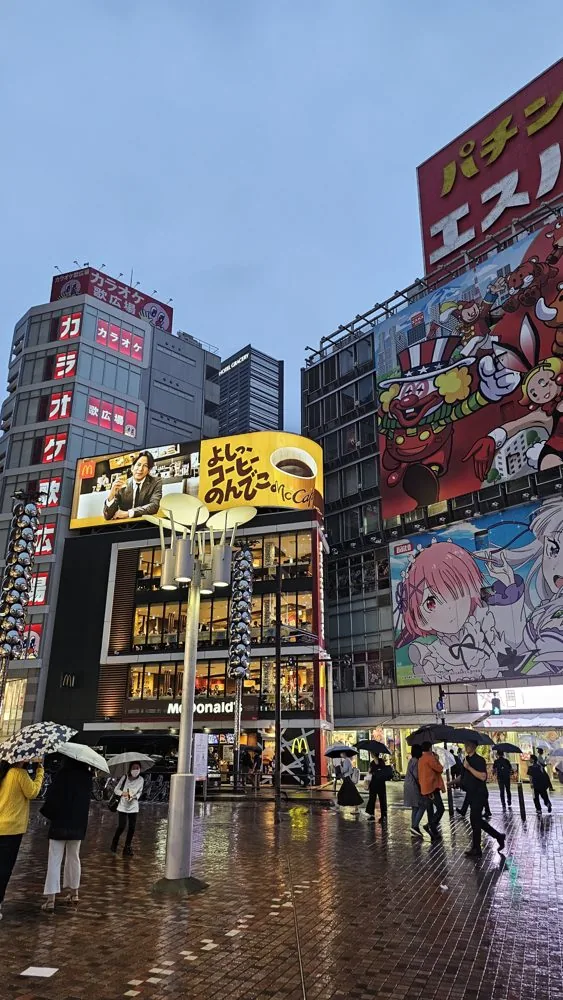 Rua de Akihabara, em Tóquio, num fim de tarde de chuva, com prédios cobertos de painéis de anime
